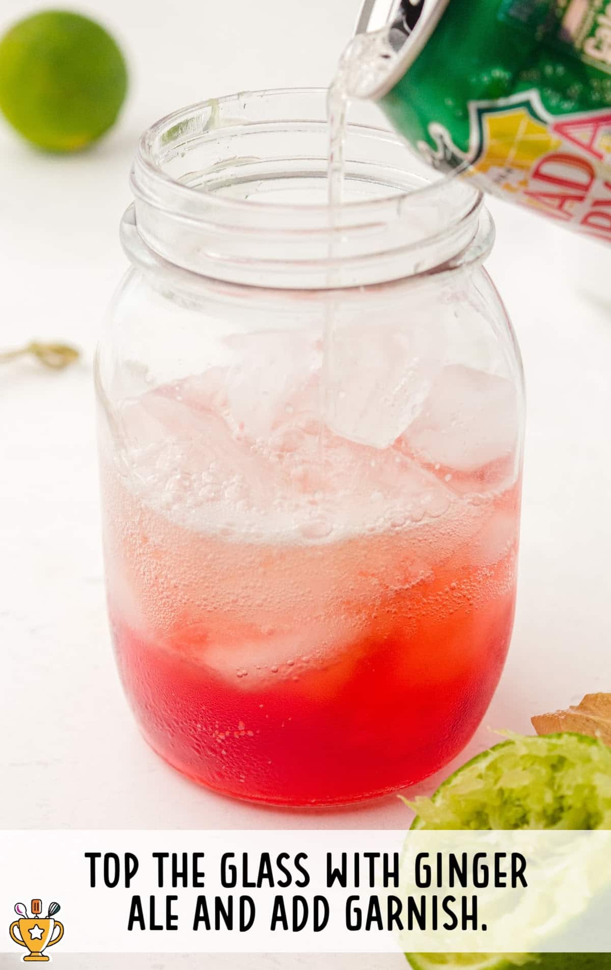 Ginger ale being poured into a mason jar over ice and grenadine, finishing off the Shirley Temple drink preparation.