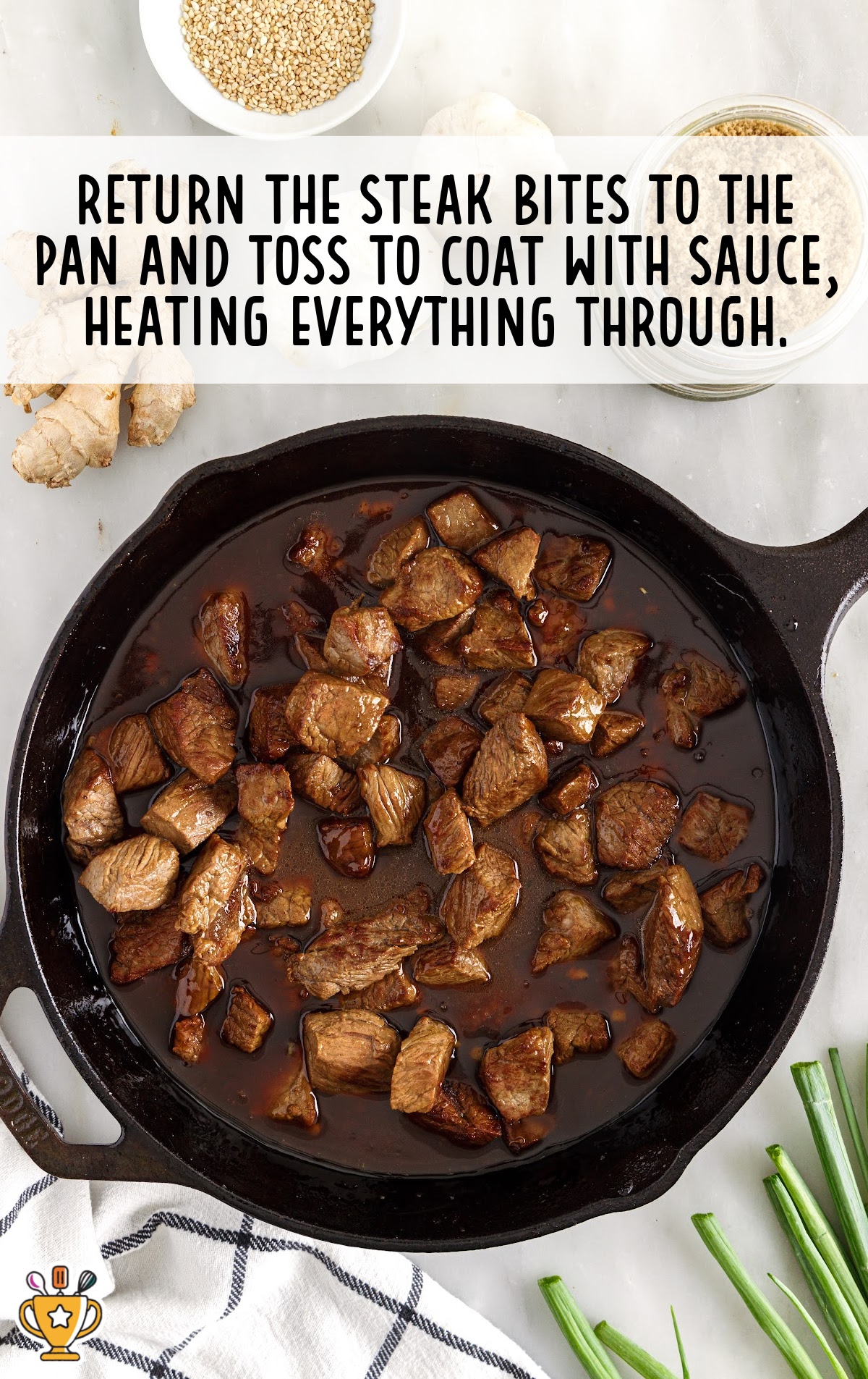 Tossing cooked steak bites in thickened teriyaki sauce inside a black skillet on a white countertop.
