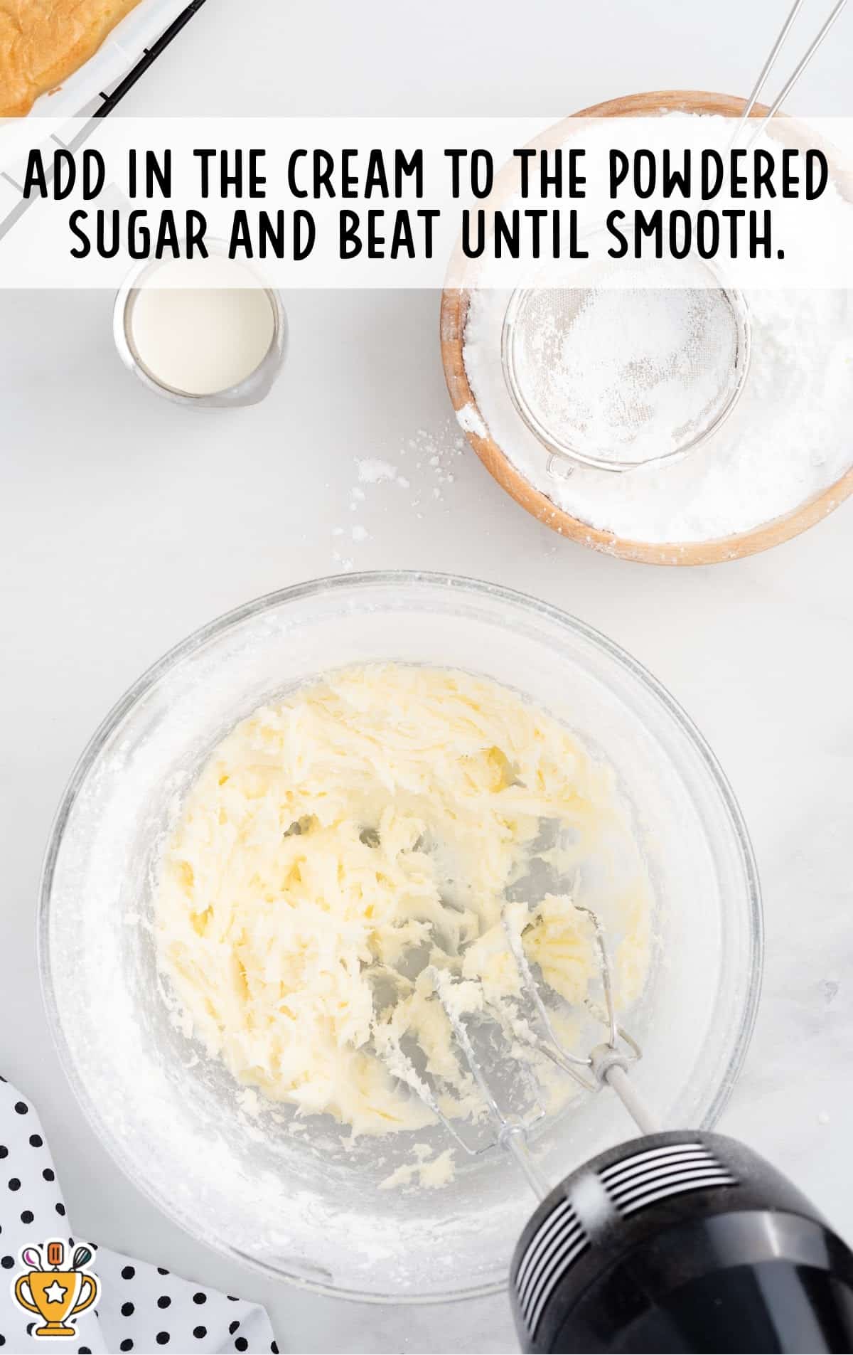 Thickened frosting mixture after cream is added to the powdered sugar and butter, shown mid-mixing in a glass bowl with a handheld mixer.
