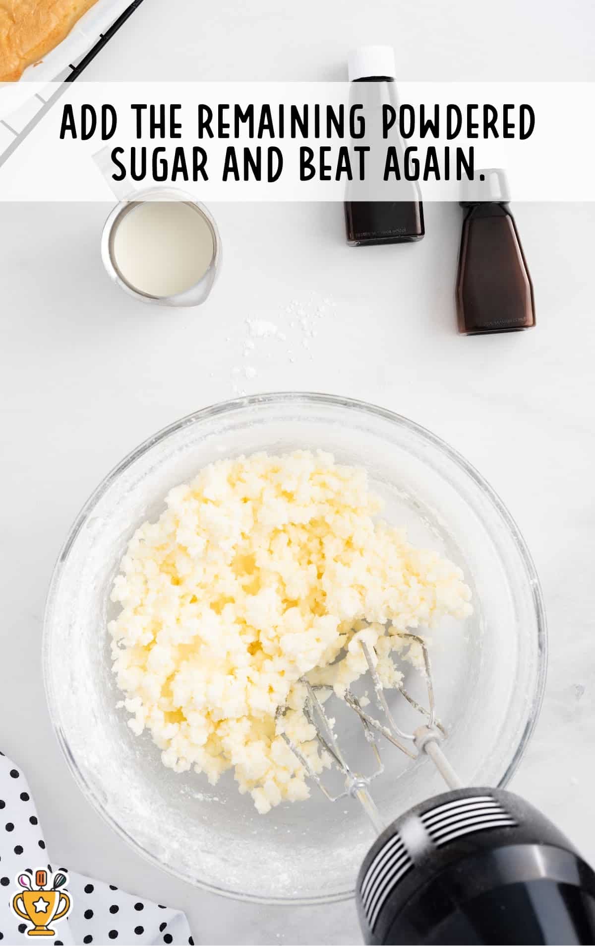 Crumbly frosting base after adding more powdered sugar, ready to be blended smooth in a clear mixing bowl with beaters.
