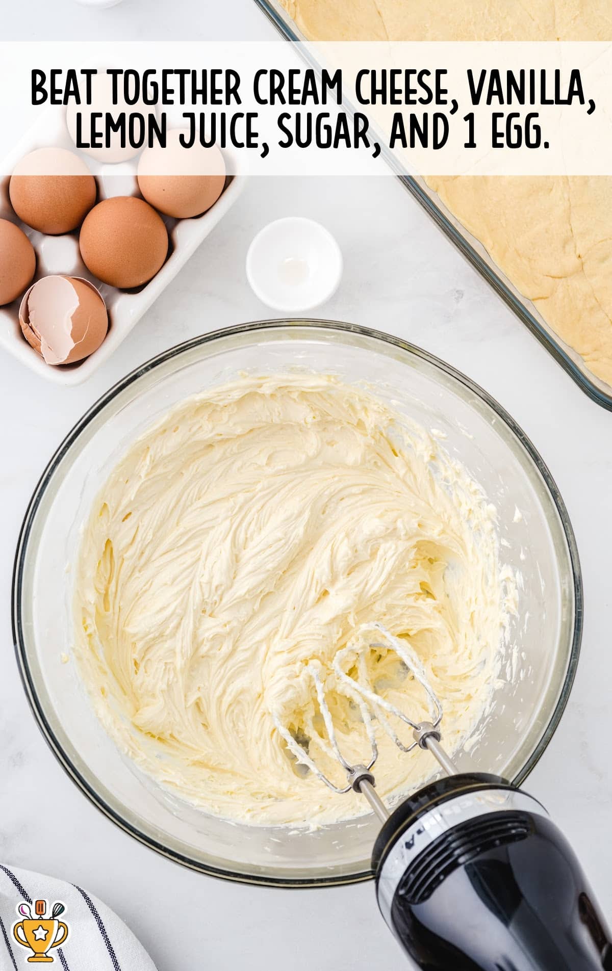 Cream cheese mixture in a glass bowl with hand mixer after blending. Eggs, lemon juice, and crescent rolls nearby. Text overlay describes ingredients used.