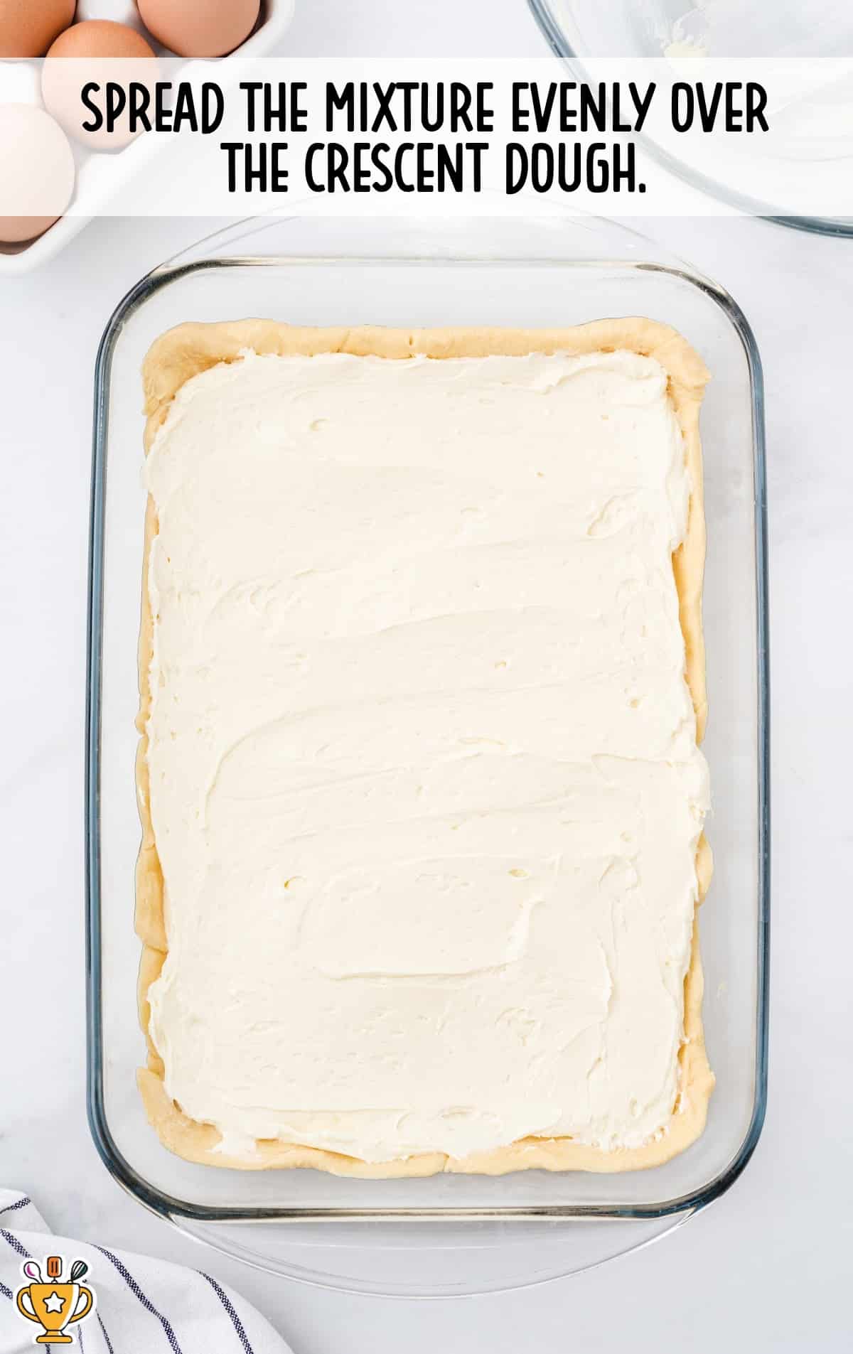 Cream cheese filling spread evenly over crescent dough in baking dish. Text overlay gives next step in recipe.