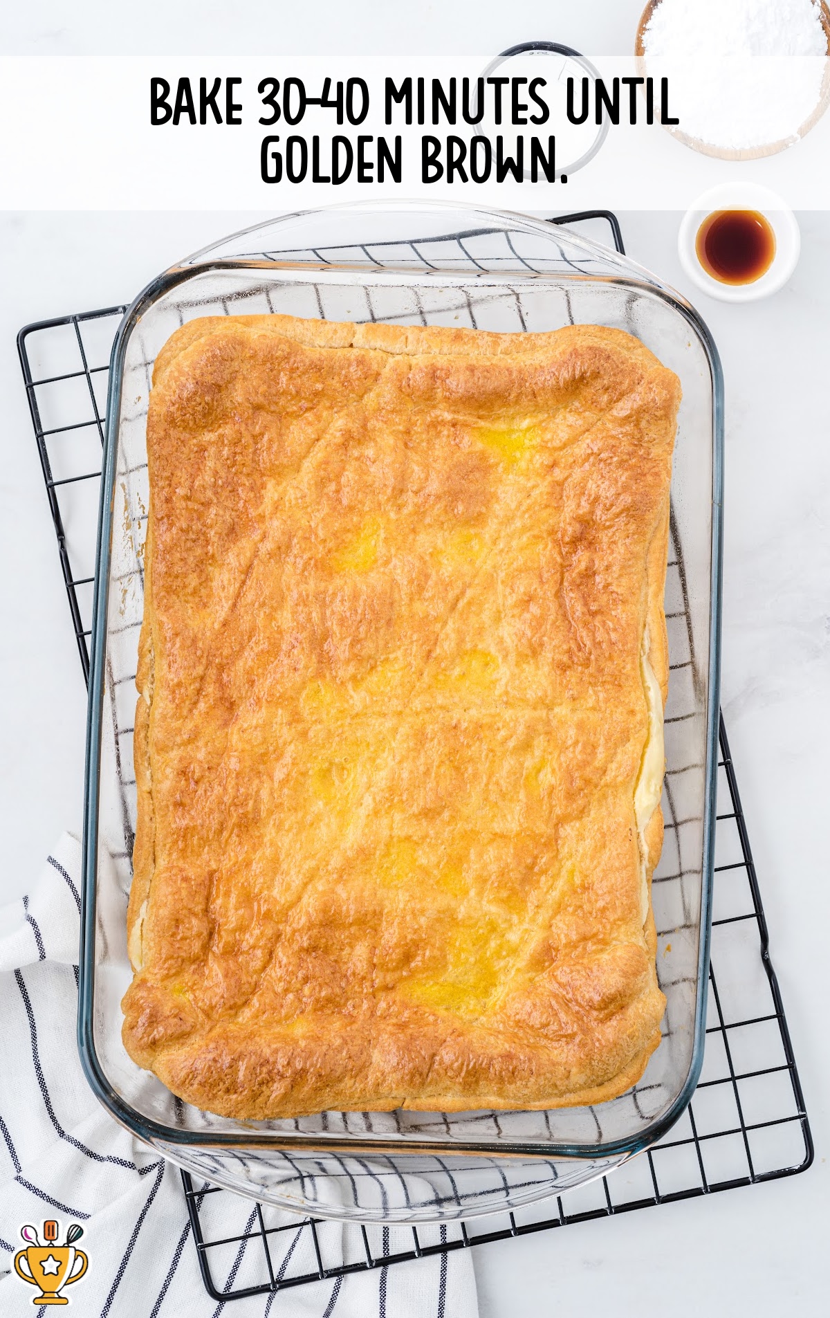 Cheese danish baked to golden brown in baking dish, resting on cooling rack. Vanilla and powdered sugar nearby. Text overlay states baking time.