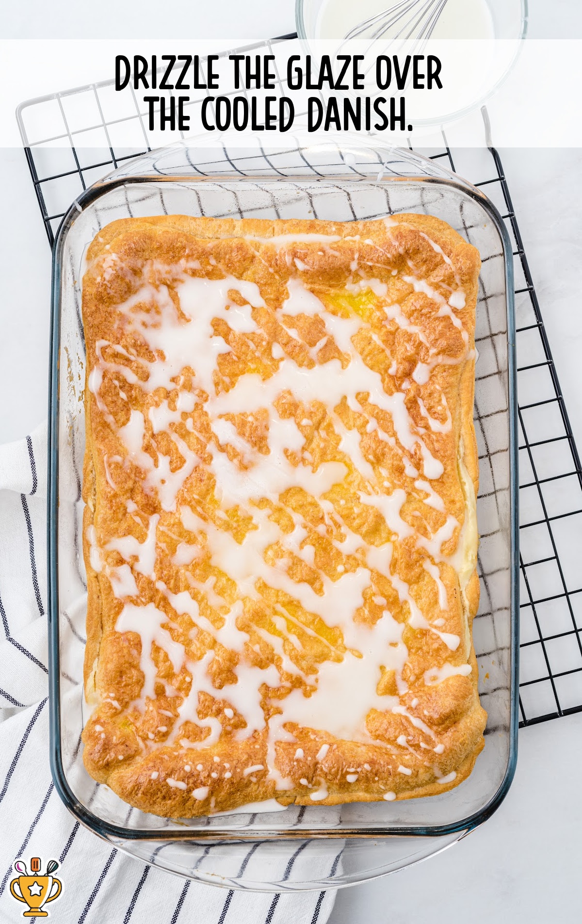Glaze drizzled over baked and cooled cheese danish in glass dish. Black and white towel underneath. Text overlay instructs to drizzle glaze.