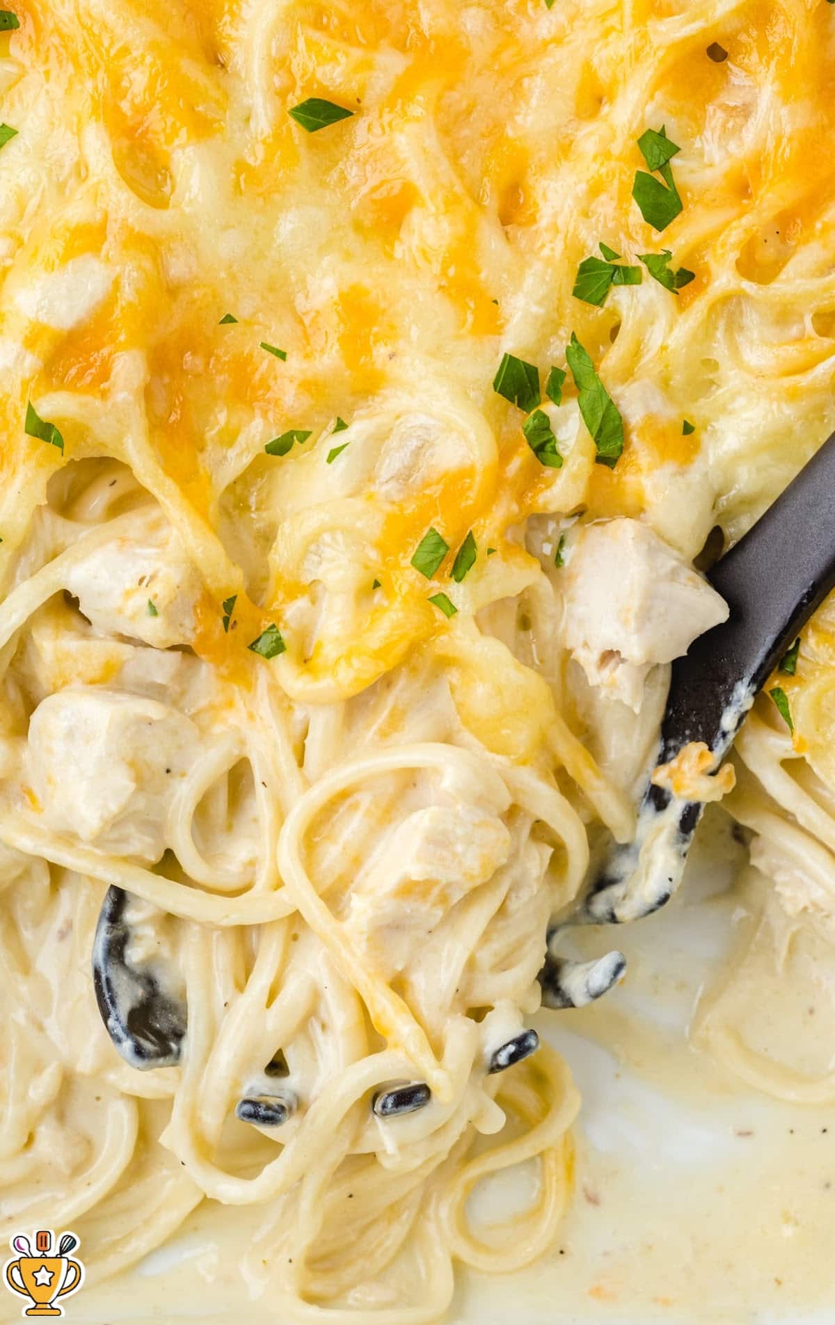 Top-down view of Chicken Tetrazzini in a white baking dish with a spoonful scooped out, revealing cheesy noodles and chicken chunks.