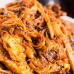 Vertical Pinterest pin with bold text overlay, showcasing a saucy close-up of shredded Dr. Pepper pulled pork in a white bowl.