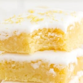 Close-up of stacked lemon brownies topped with a sweet white glaze and sprinkled with fresh lemon zest.