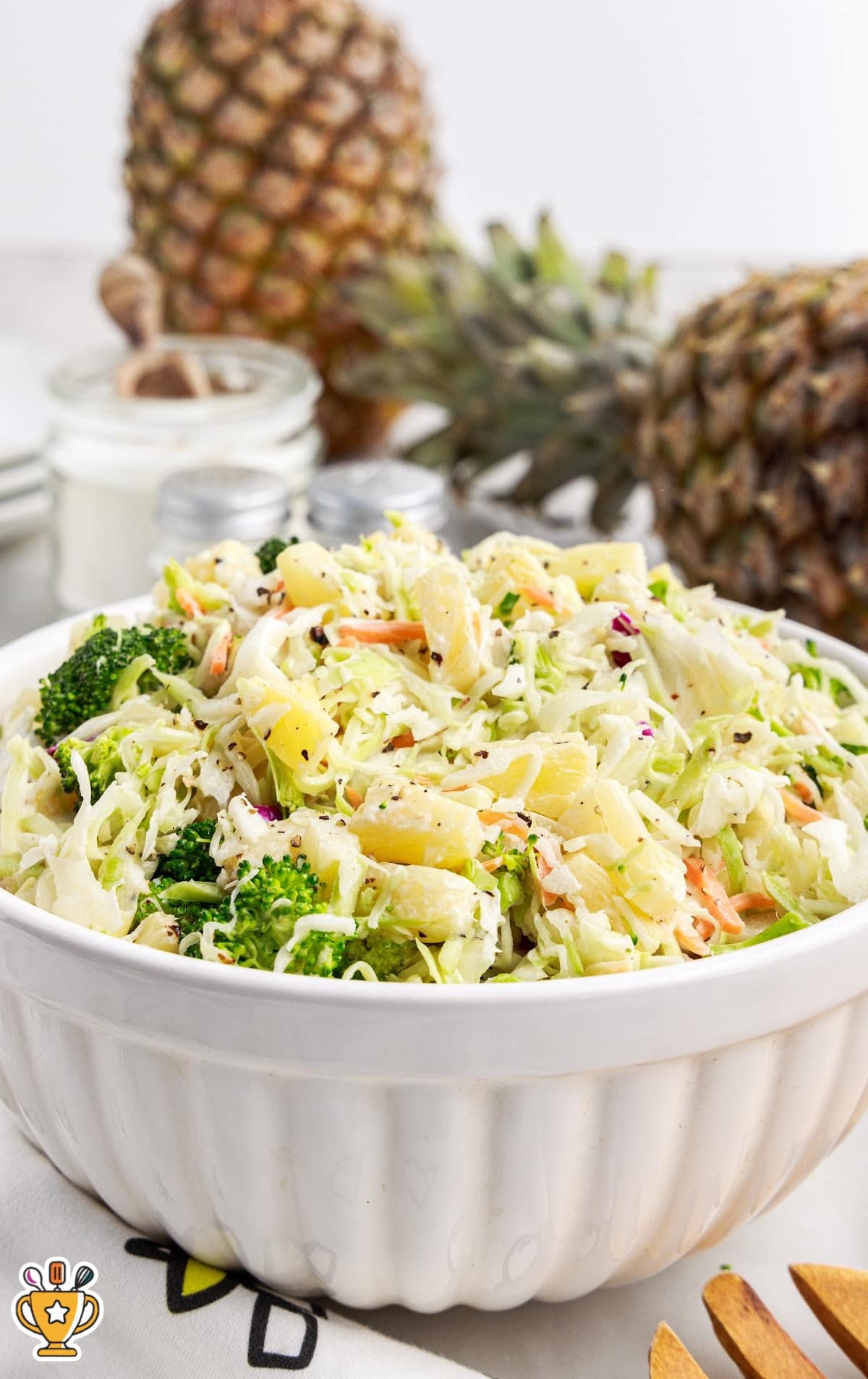 Pineapple coleslaw served in a white bowl with fresh pineapples in the background, ready to be served as a side dish.