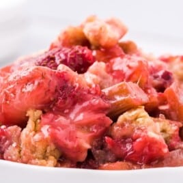 Close-up of a serving of rhubarb strawberry crisp on a white plate, showing gooey fruit filling and golden crumble topping.