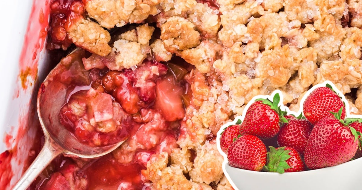Overhead shot of rhubarb strawberry crisp in a baking dish with a large spoonful scooped out and strawberries in the corner.