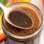 Close-up of a jar filled with homemade 3-ingredient stir fry sauce, with a spoon resting on top showing the glossy, dark brown sauce with oil droplets on the surface.