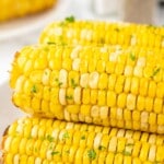 Close-up of air fryer corn on the cob topped with melted butter and parsley, golden yellow kernels perfect for an easy summer side dish