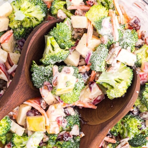 Broccoli Apple Salad in a clear bowl with two wooden spoon in it