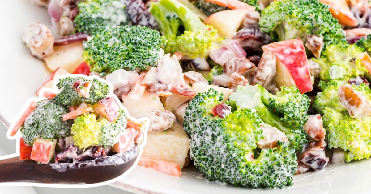 a wooden spoon holding some Broccoli Apple Salad and a plate full of Broccoli Apple Salad