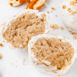 Close-up of butter pecan cheesecake bites on a white plate, with one bite cut in half to show a soft, creamy interior, surrounded by chopped pecans.