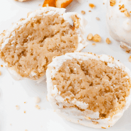 Close-up view of butter pecan cheesecake bites cut in half, showing the creamy, soft interior coated in white almond bark and topped with chopped pecans.