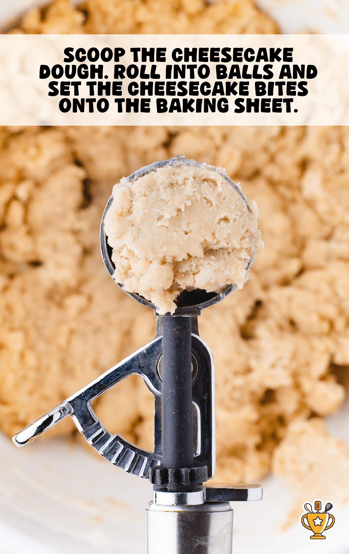 Cookie scoop holding a ball of butter pecan cheesecake dough above a mixing bowl, with soft, crumbly dough in the background.