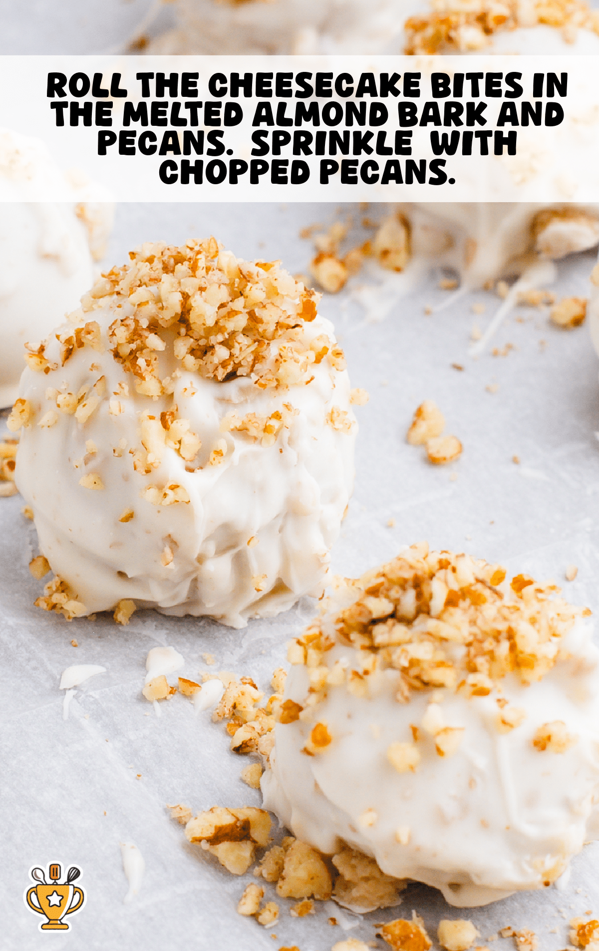 Close-up of butter pecan cheesecake bites coated in white almond bark and topped with chopped pecans, displayed on parchment paper with crumbs scattered around.