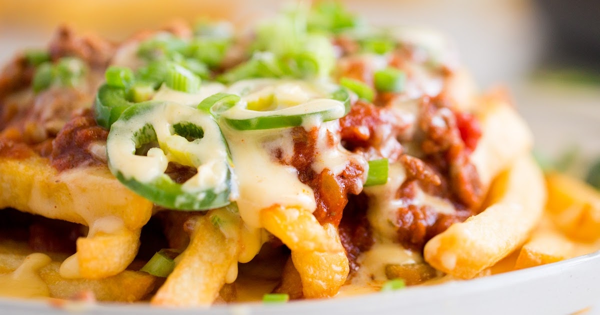 Close-up of golden fries drenched in chili and gooey cheese, with spicy jalapeños and chopped green onions on top.
