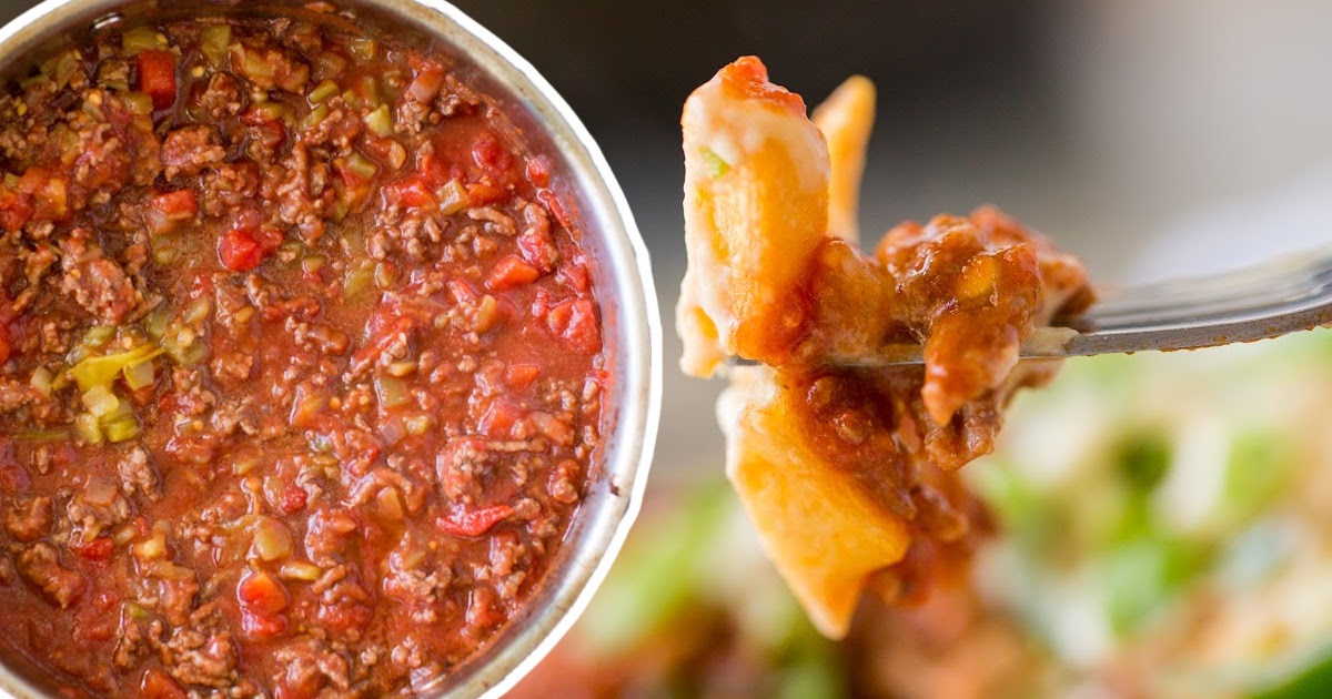 Spoonful of loaded chili cheese fries held above a pot of hot beef and bell pepper chili, ready to be served.