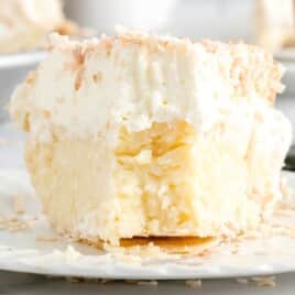 Classic coconut cream pie with golden flaky crust and whipped cream topping, served on a white plate.