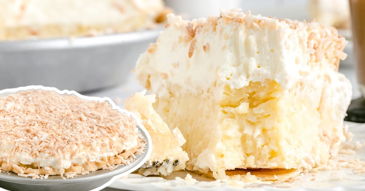 Coconut cream pie slice on a dessert plate with fork, surrounded by coconut flakes.