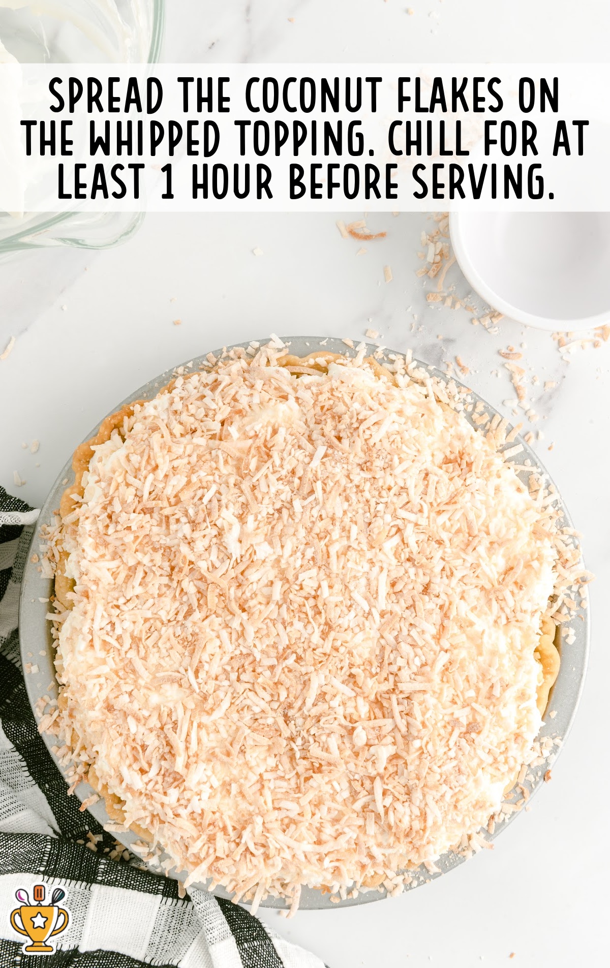 Coconut flakes spread on top of the whipped cream layer of a coconut pie, ready to chill.