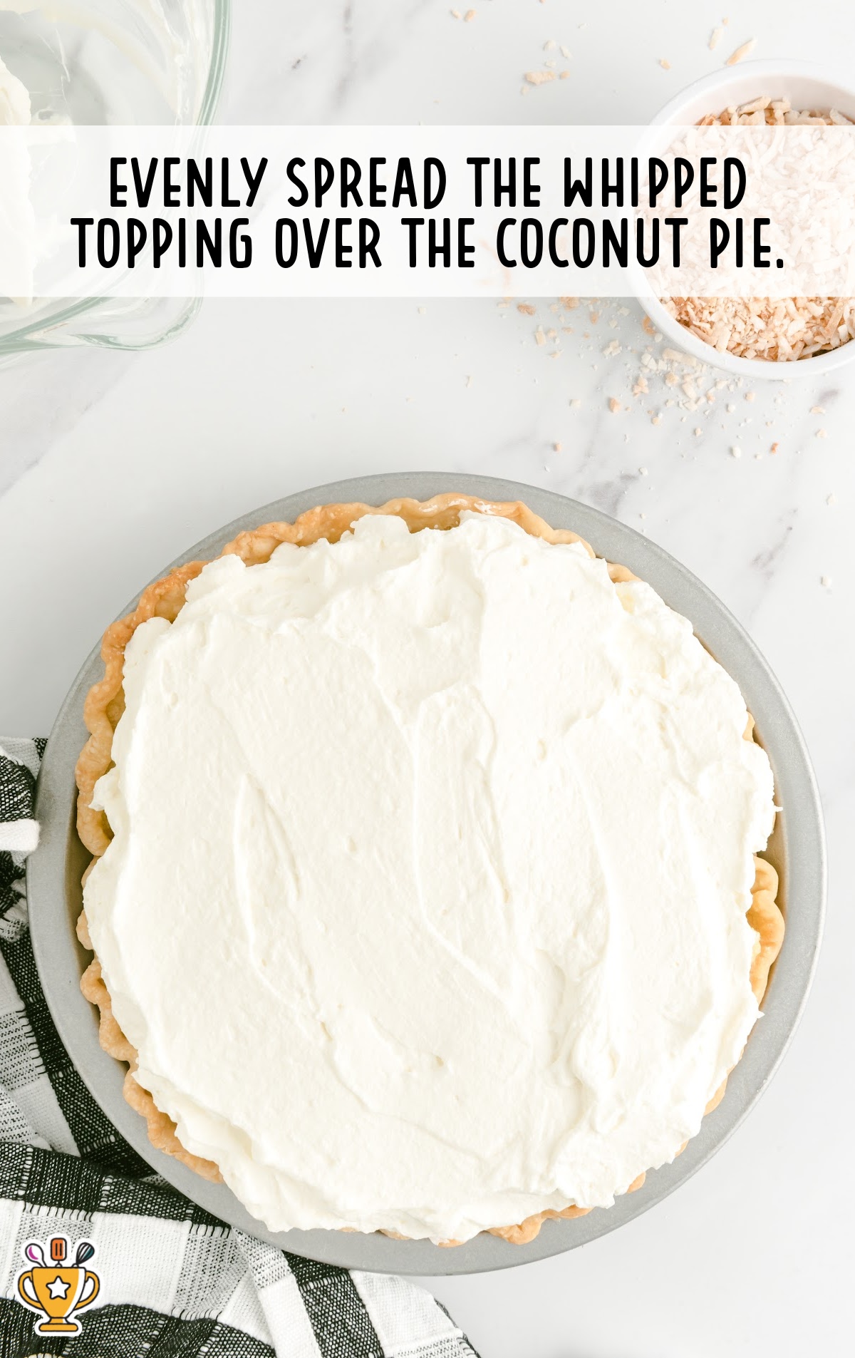 Whipped topping evenly spread over a coconut pie in a metal pie plate on a marble counter.