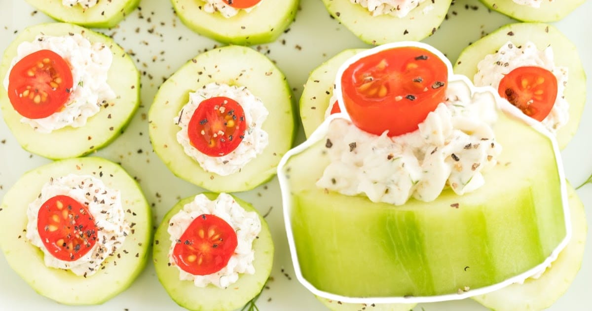 Close-up view of cucumber bites topped with a creamy filling and halved cherry tomatoes, garnished with cracked pepper.