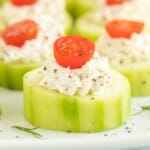 Square-format photo showing a perfectly assembled cucumber bite with creamy herbed filling and a cherry tomato, ideal for a recipe card graphic.