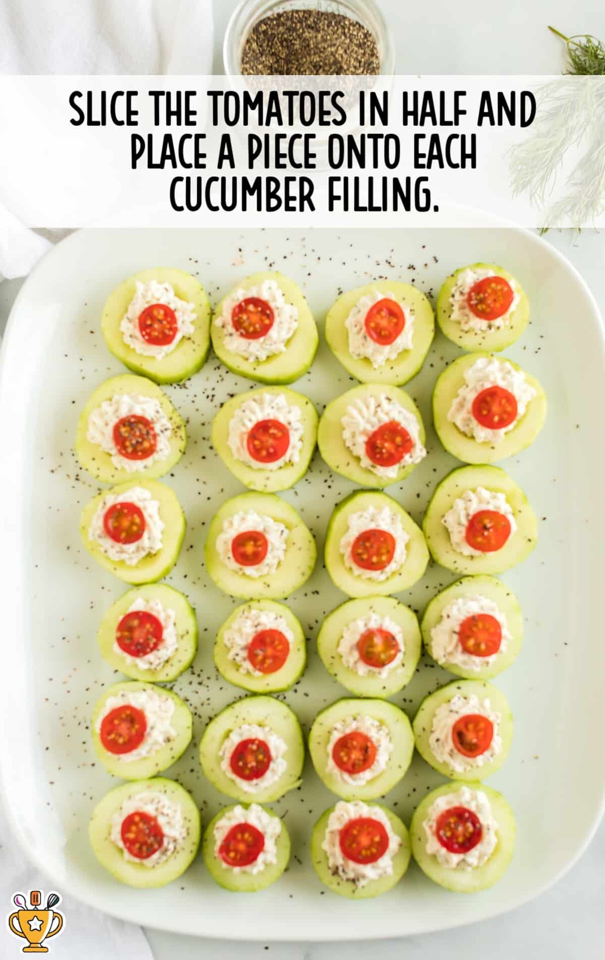 Cucumber bites arranged on a platter with creamy filling and halved cherry tomatoes placed on top of each one.