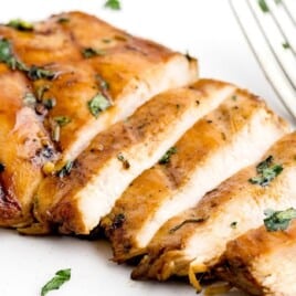 Single sliced grilled chicken breast on a white plate with a fork, garnished with chopped herbs.