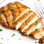 Raw ingredients for the marinade arranged around chicken breasts, including beer, soy sauce, honey, olive oil, garlic, and cilantro.