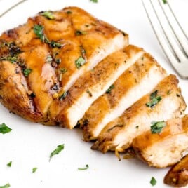 Raw ingredients for the marinade arranged around chicken breasts, including beer, soy sauce, honey, olive oil, garlic, and cilantro.