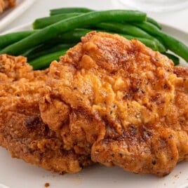 A delicious fried pork chop with a crispy golden crust, placed on a plate with a side of green beans for a perfect meal.
