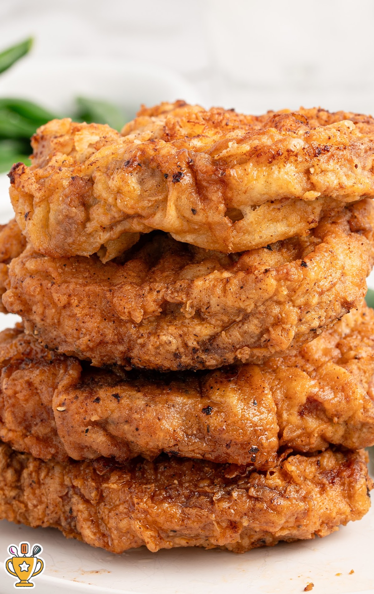 A stack of crispy fried pork chops with a golden brown exterior and tender inside, served with green beans on the side.