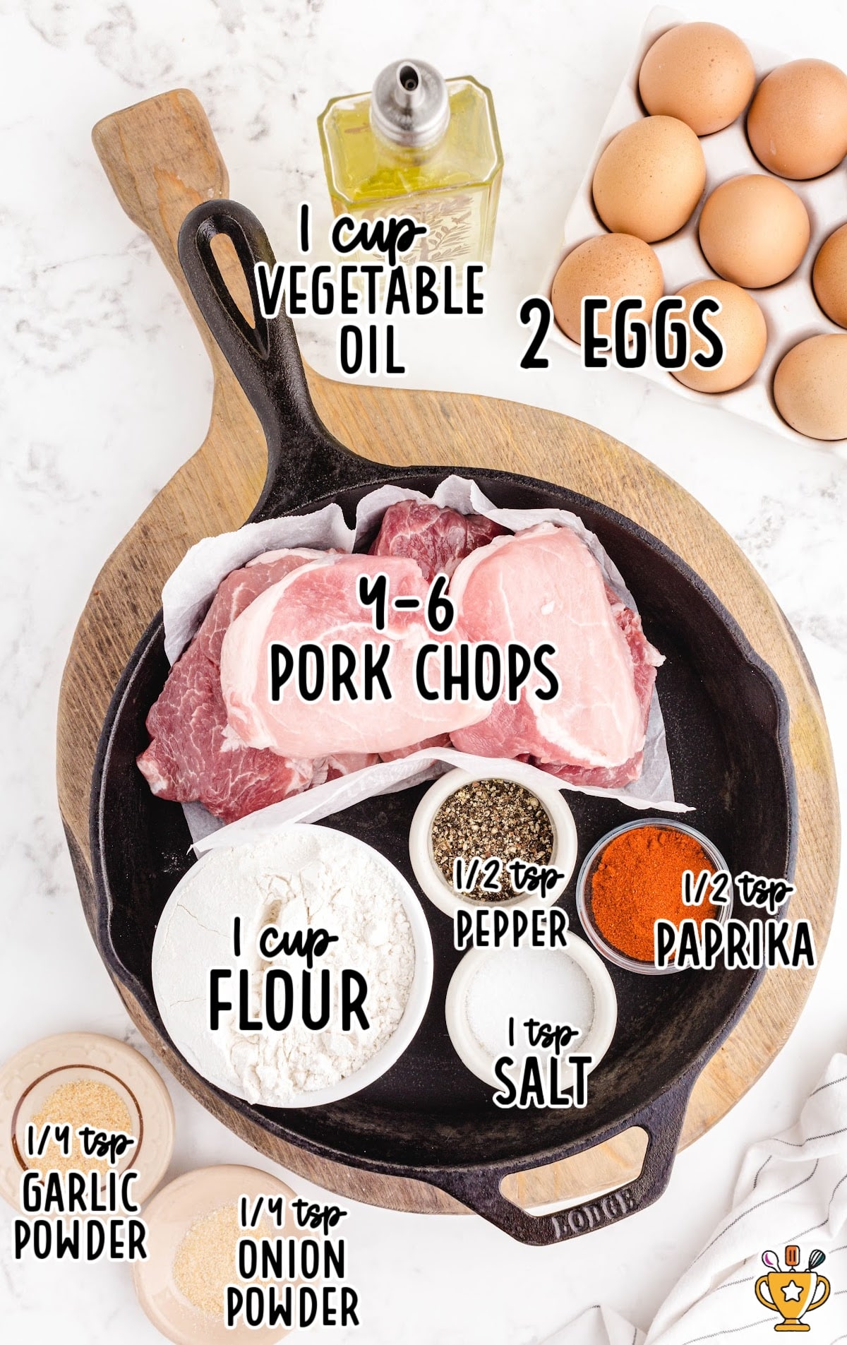 Ingredients for pan-fried pork chops: pork chops, flour, pepper, salt, paprika, garlic powder, onion powder, eggs, and vegetable oil, arranged in a skillet and on a wooden board.