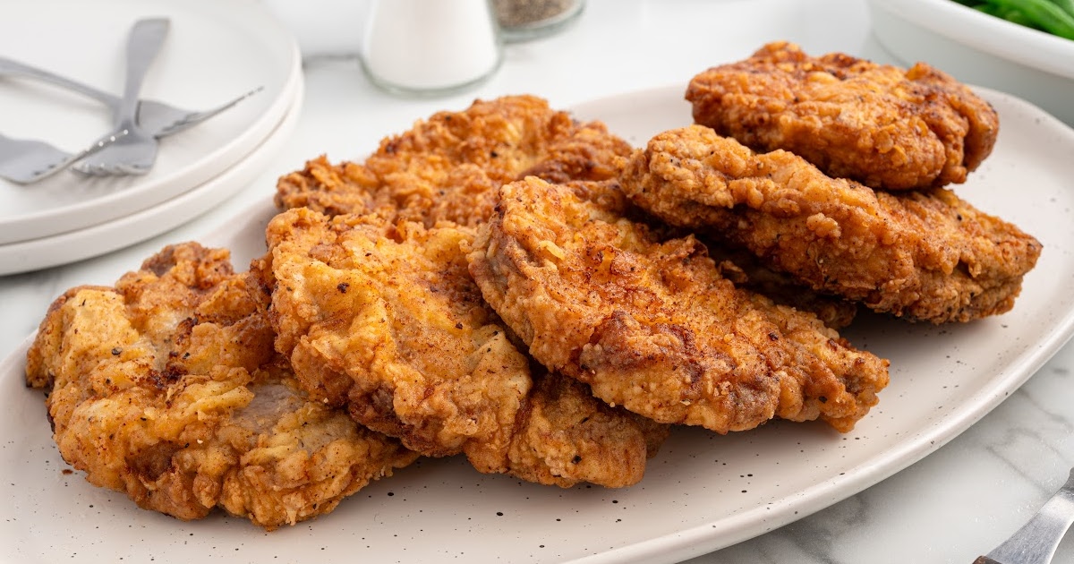 A plate of crispy, pan-fried pork chops served with green beans, showcasing their golden crust and tender interior.