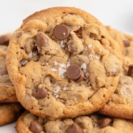 A close-up of freshly baked gluten-free chocolate chip cookies with a soft center and crispy edges on a baking sheet. The image highlights the texture and golden color of the cookies.
