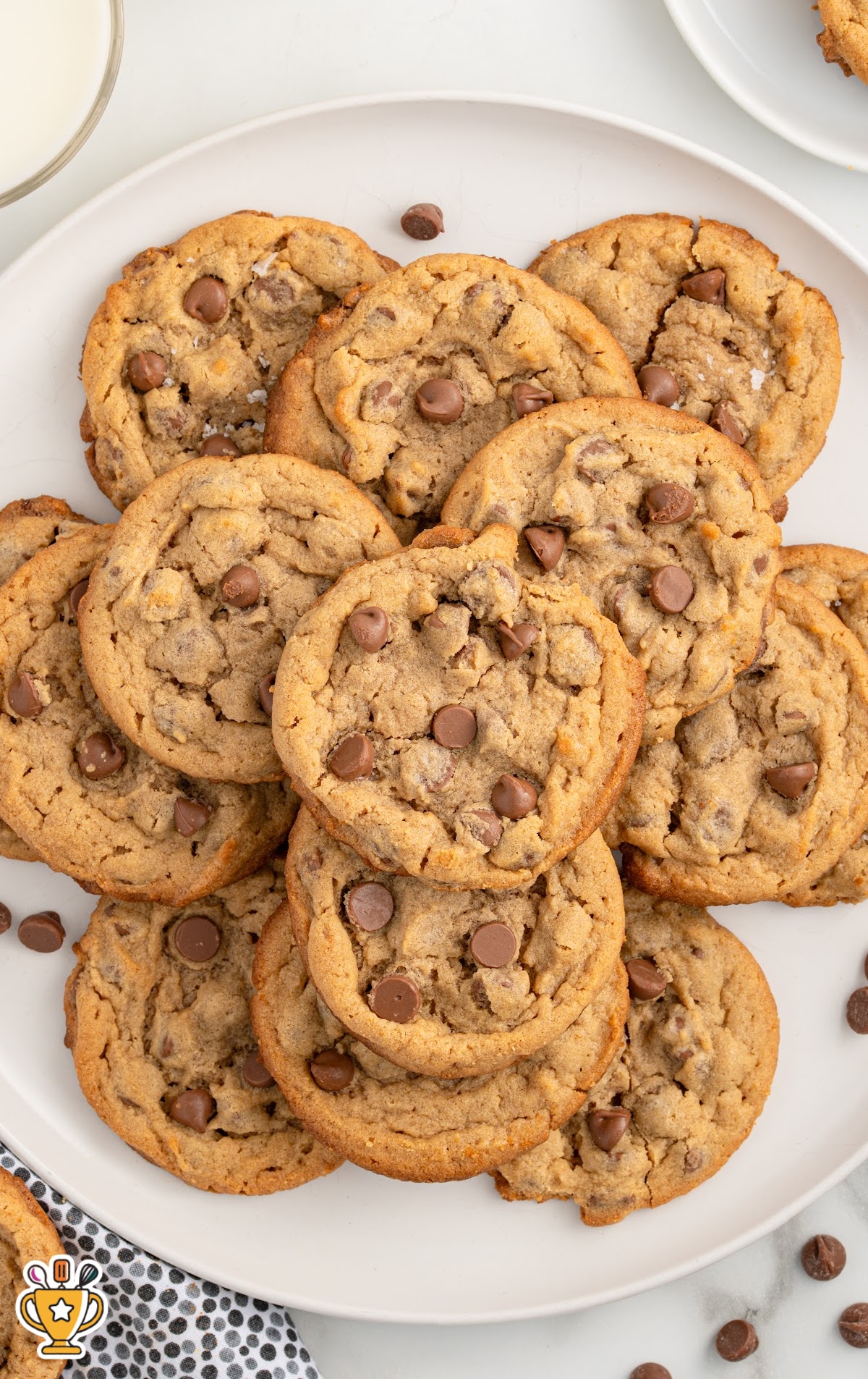 A stack of gluten-free chocolate chip cookies with a few broken in half, showing the gooey chocolate chips inside. The cookies are arranged on a plate with a slightly blurred background.