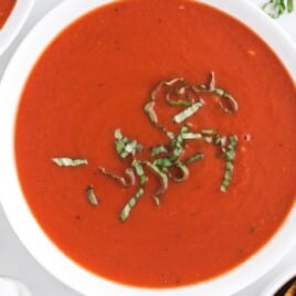 A vibrant bowl of homemade tomato soup garnished with basil, placed on a rustic wooden board.
