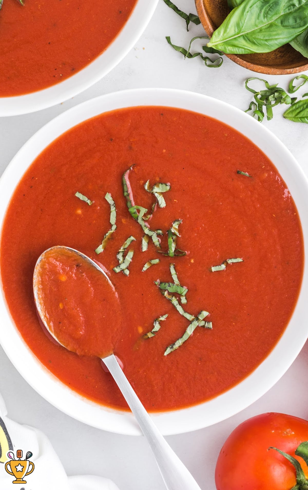 A close-up of a bowl of homemade tomato soup topped with freshly chopped basil, with a spoon inside the soup.