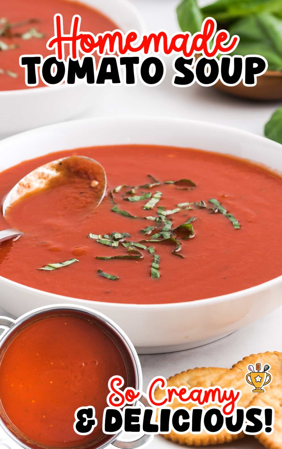 A cozy image of homemade tomato soup in a bowl, topped with basil, and served with crackers on the side.
