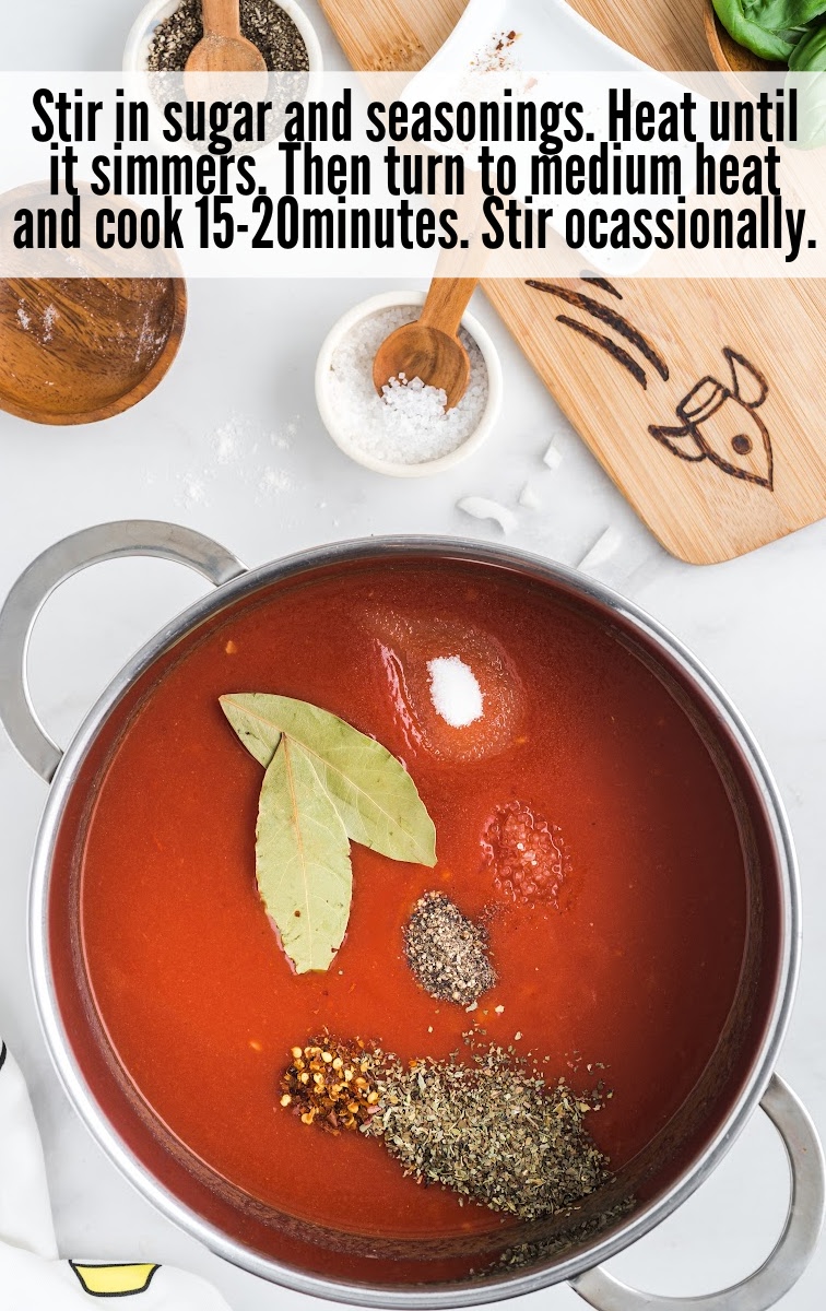 A close-up of a cooking pot with tomato soup, seasoned with bay leaves, salt, pepper, and other spices, before being stirred.