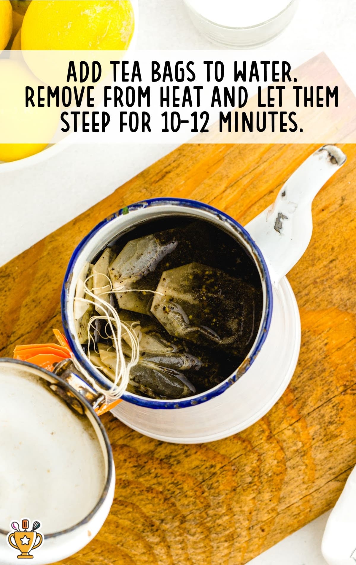 A teapot with tea bags steeping in hot water, with lemons and sugar placed around the teapot.