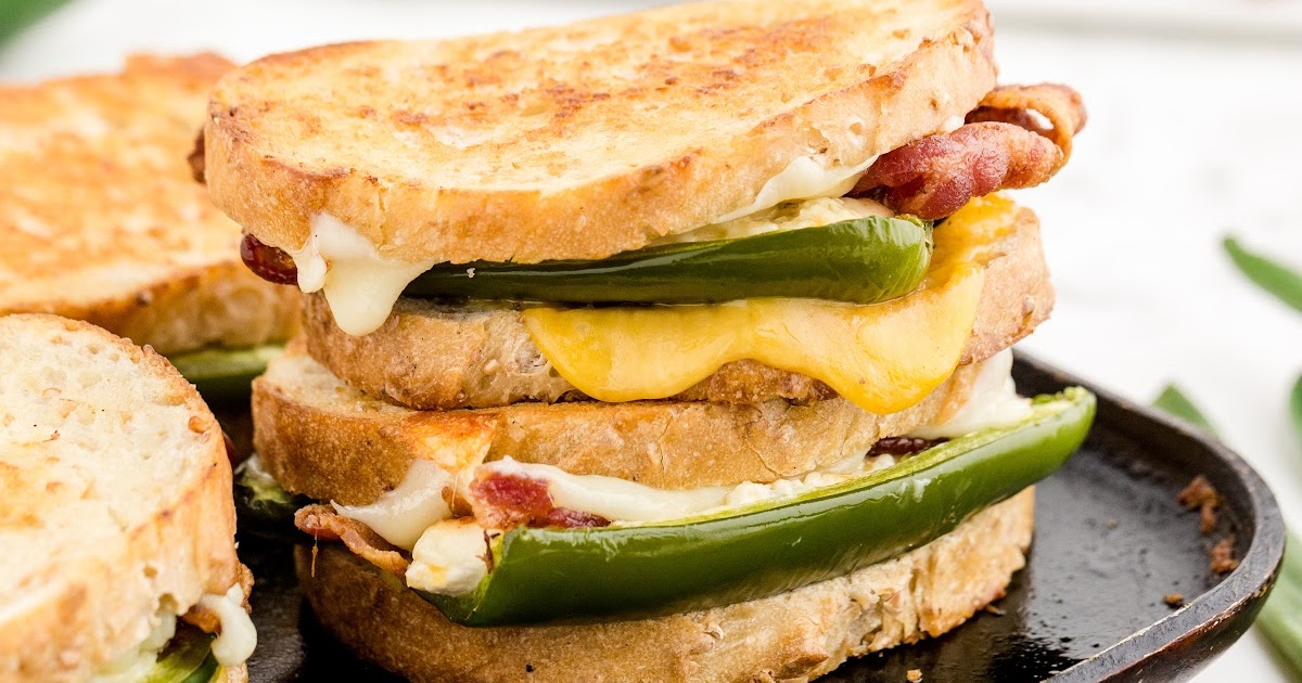 Melted cheese dripping from toasted sandwich stacked with bacon and jalapeños, with more sandwiches in the background.