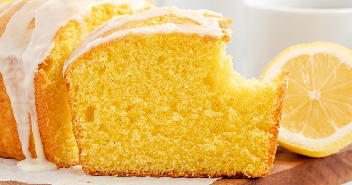 A whole glazed lemon pound cake loaf , with one slice showing a bite taken out.
