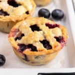 Golden blueberry pies in a muffin tin with bubbling filling, topped with coarse sugar, fresh from the oven and still warm.