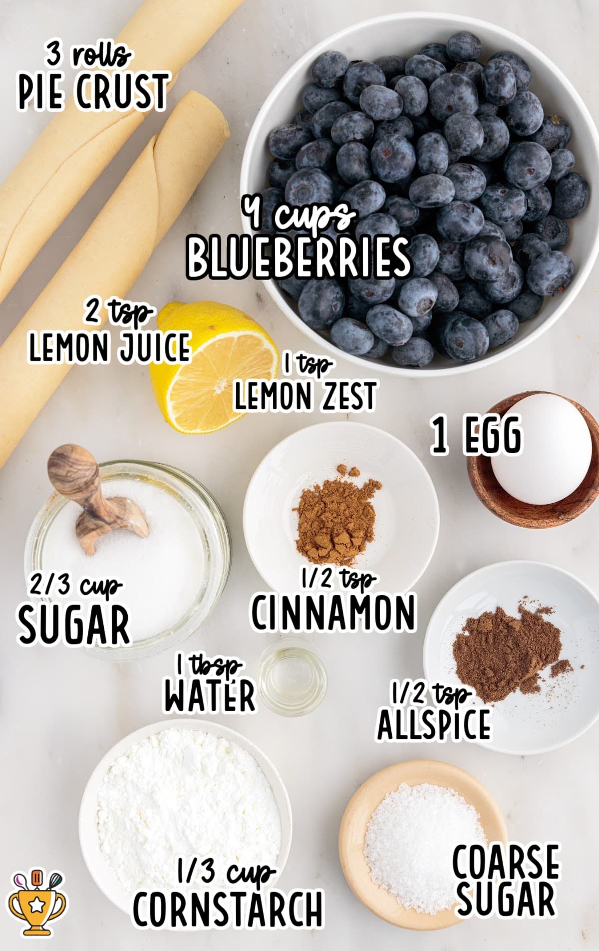 Flat lay photo of labeled ingredients for mini blueberry pies, including pie crusts, fresh blueberries, lemon, sugar, cornstarch, cinnamon, allspice, and an egg