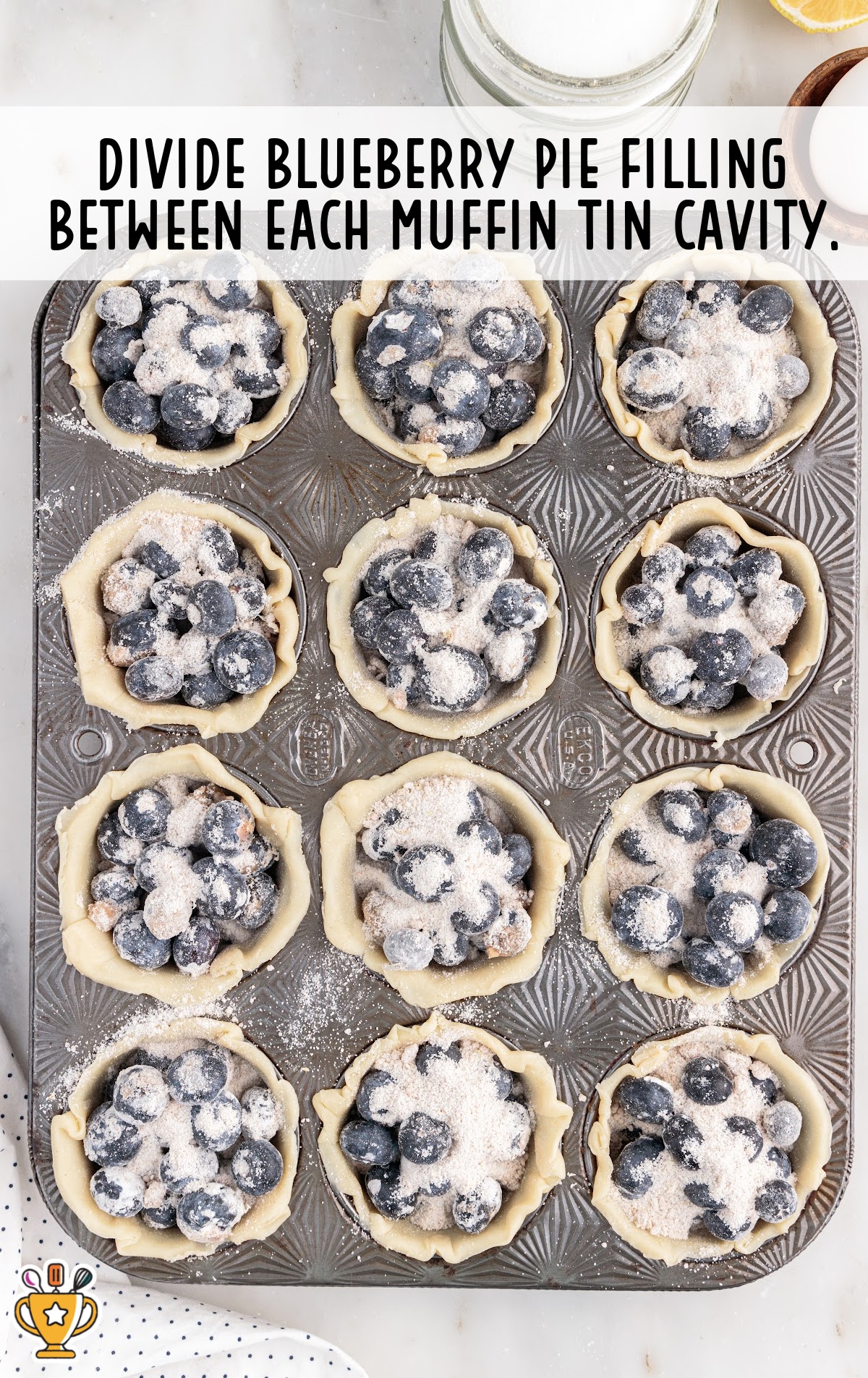 Each muffin tin cavity filled with blueberry pie mixture, showing the sugar and cornstarch coating the berries.